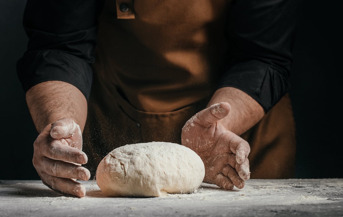 Baker's hands shaping raw dough on a floured table with dramatic light